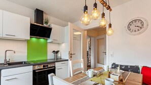 A modern kitchen with white cabinets, a green backsplash, and a dining area with a wooden table and chairs.