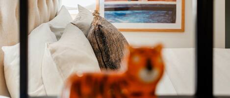 A bed with a tufted headboard, a framed picture on the wall, and a small orange toy on the bedside table.