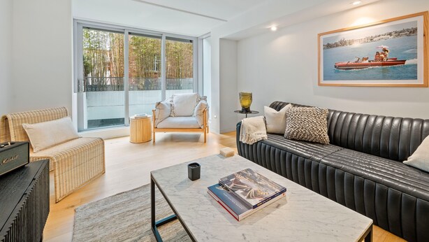 A modern living room with a sofa, a chair, a coffee table, and a large window with a view of trees. - Bondi Pacific Studio - Managed by X Hospitality (Bondi Beach)