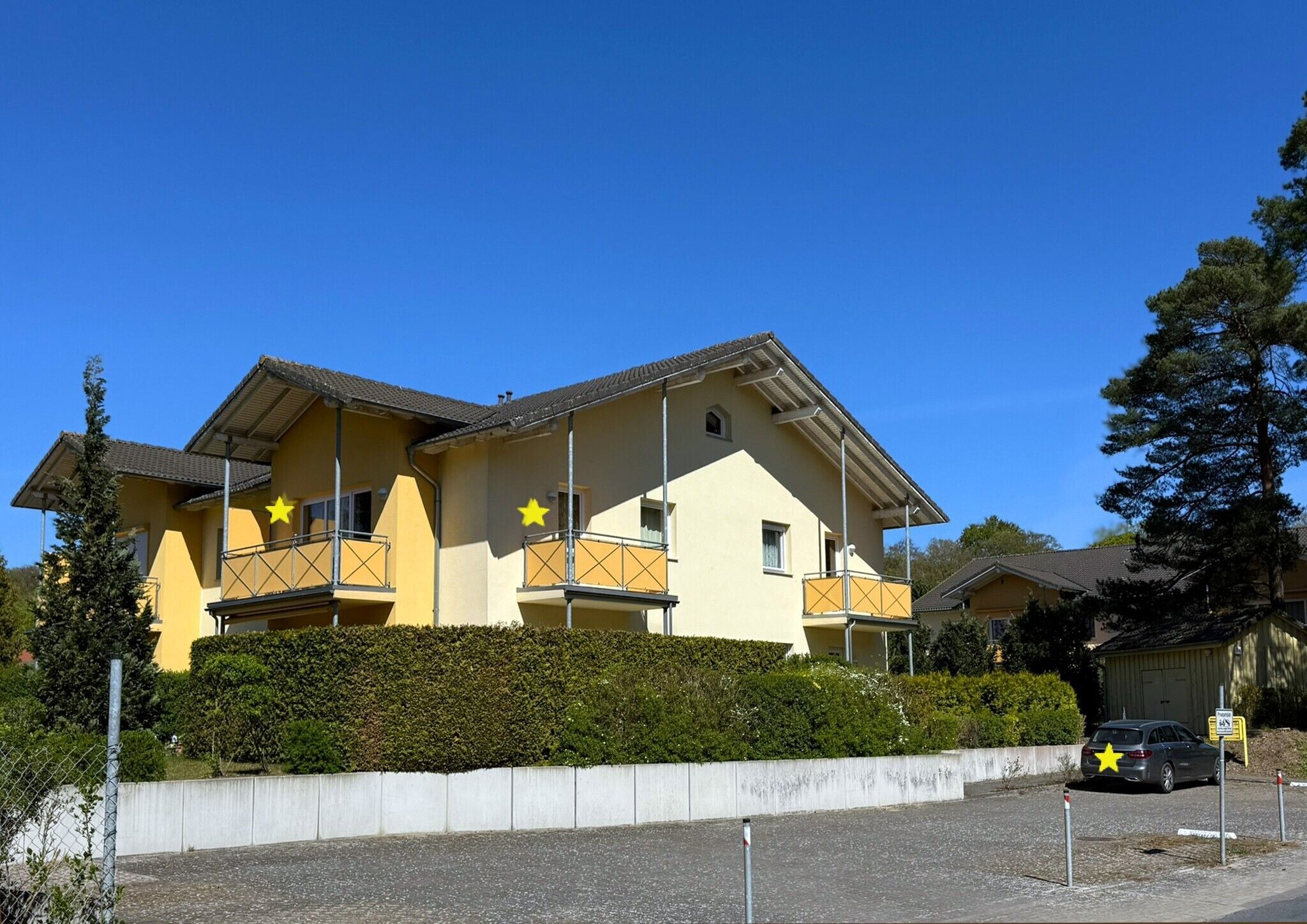 A two-story building with balconies, a parking area, and a hedge in front.