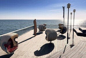 Eine Holzterrasse mit Sitzbereichen und Geländer mit Blick auf ein Gewässer.