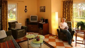 A living room with a sofa, armchair, television, and a table with a bowl of fruit. - Apartment "Melosine" with Balcony (Koserow)