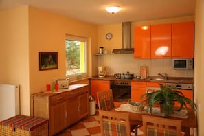 A kitchen with orange cabinets, a stove, microwave, and a dining area with a table and chairs.