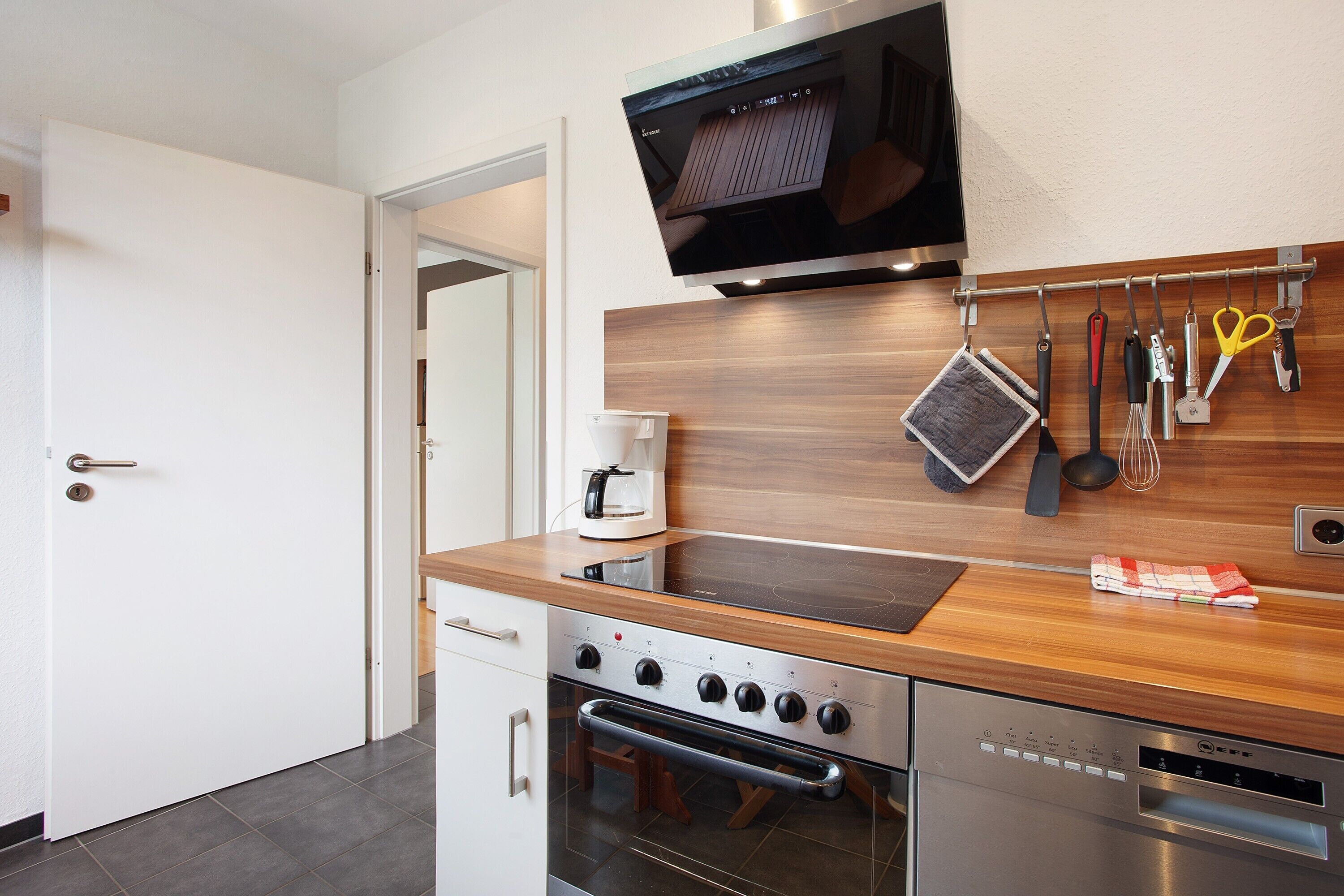 A modern kitchen with a built-in oven, a coffee machine, and a TV mounted above the counter.