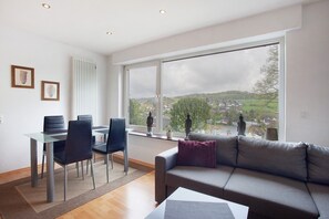 Una sala de estar moderna con un sofá, una mesa de comedor con sillas y un gran ventanal con vistas a un pueblo.