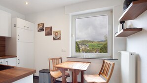 A kitchen with a window view, wooden chairs, a table, and a trash bin. - Apartment "Keil" with Mountain View, Private Terrace & Wi-Fi (Balve)