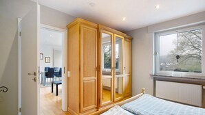 A bedroom with a bed, a wooden wardrobe, a window with a view, and a door leading to a dining area. - Apartment "Keil" with Mountain View, Private Terrace & Wi-Fi (Balve)