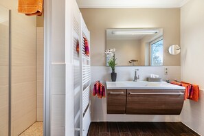 Un baño moderno con ducha, tocador con espejo y una orquídea en maceta.