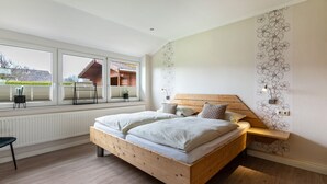 Une chambre à coucher avec un lit en bois, une fenêtre avec des stores, un radiateur et un luminaire fixé au mur.