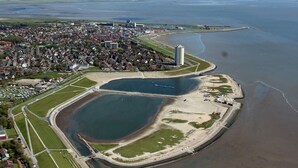 Une vue aérienne d’une ville côtière, avec des zones résidentielles, une étendue d’eau importante et un bâtiment remarquable.