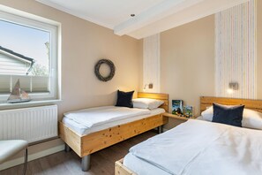 Un dormitorio con dos camas, una ventana con persianas, un radiador, un arreglo colgante en la pared y una mesita de noche con lámpara.