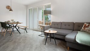 A modern living room with a grey sofa, a round wooden table, and a dining area with chairs.
