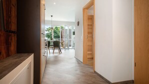 A hallway with a wooden door, a dining area with a table and chairs, and a view of the outdoors.