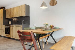 A modern kitchen with wooden cabinets, a built-in oven, and a dining table set with plates, bowls, and glasses.