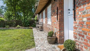 A brick house with a thatched roof, a stone pathway, and a small garden with a bench and potted plants. - Holiday Home "Luis - Hus" with 2 Private Terraces, Garden, and Wi-Fi (Dagebüll)