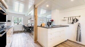 A modern kitchen with white cabinetry, a central island, and a dining area with a table and chairs. - Holiday Home "Luis - Hus" with 2 Private Terraces, Garden, and Wi-Fi (Dagebüll)