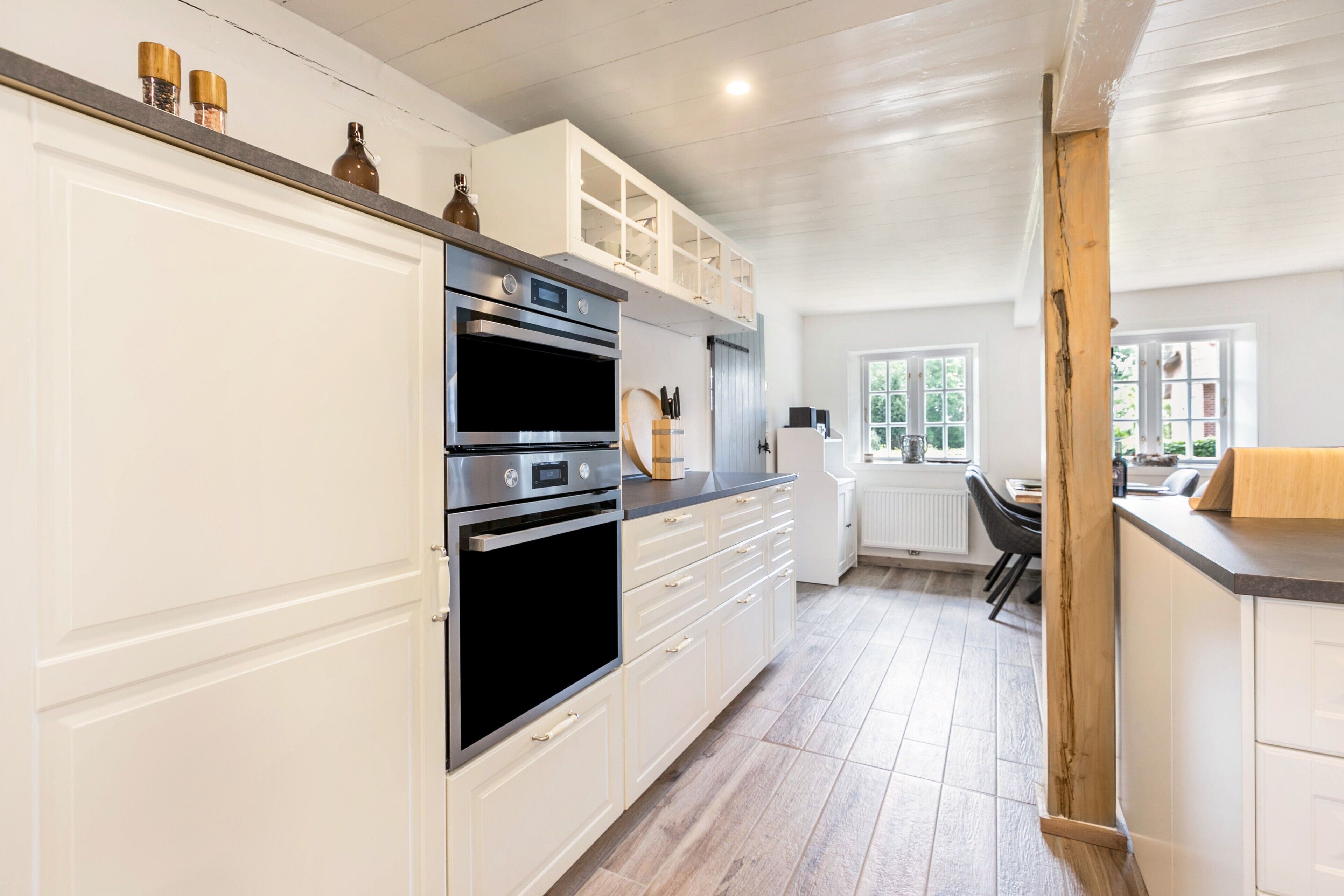 A kitchen with white cabinets, a double oven, and a countertop with kitchen utensils.
