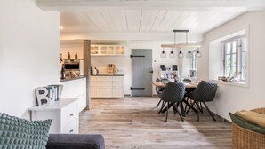 A modern kitchen with white cabinets, a dining area with a table and chairs, and a cozy seating area with a sofa and cushions. - Holiday Home "Luis - Hus" with 2 Private Terraces, Garden, and Wi-Fi (Dagebüll)