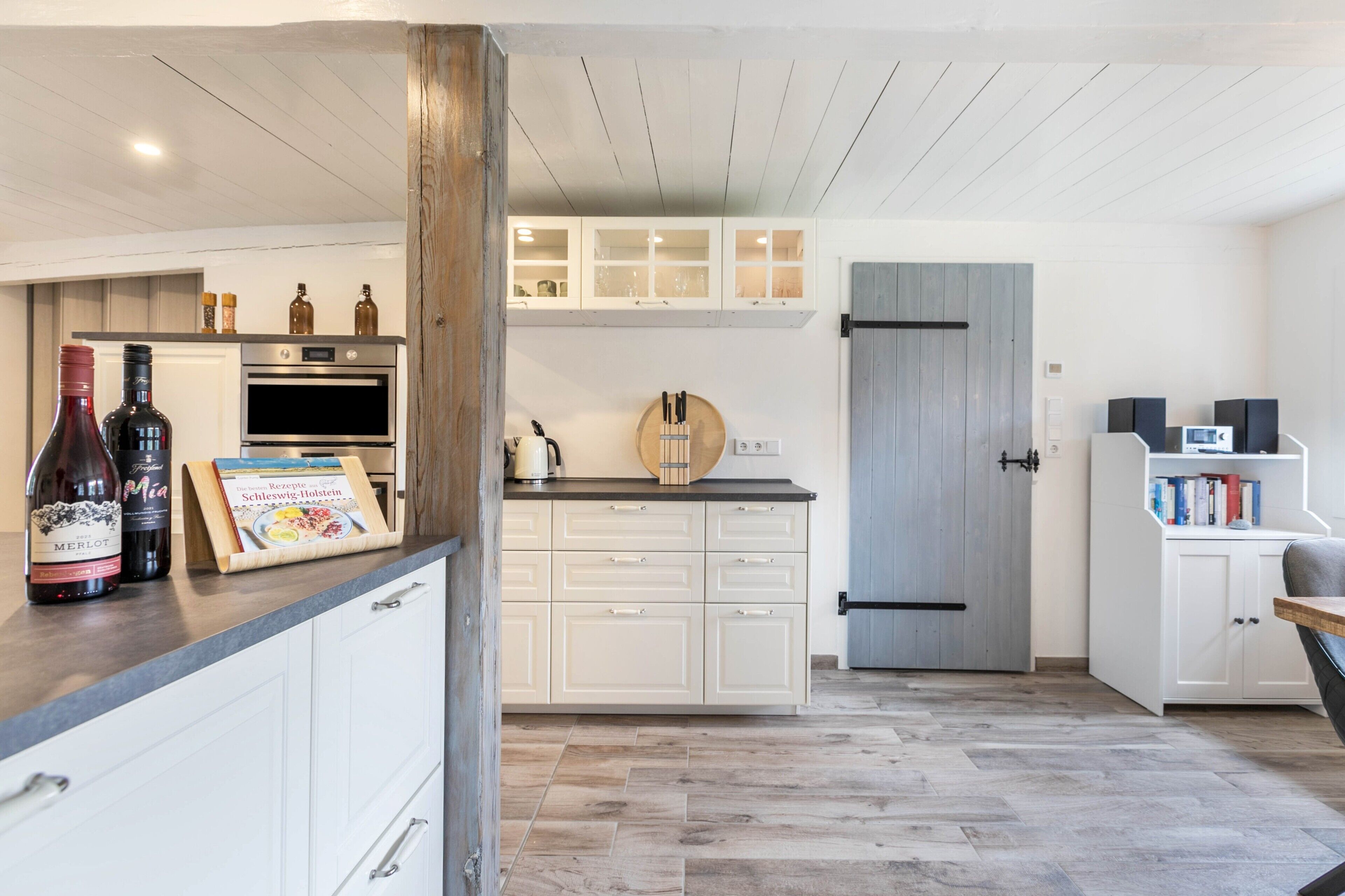 A modern kitchen with white cabinetry, a built-in oven, and a wooden door.