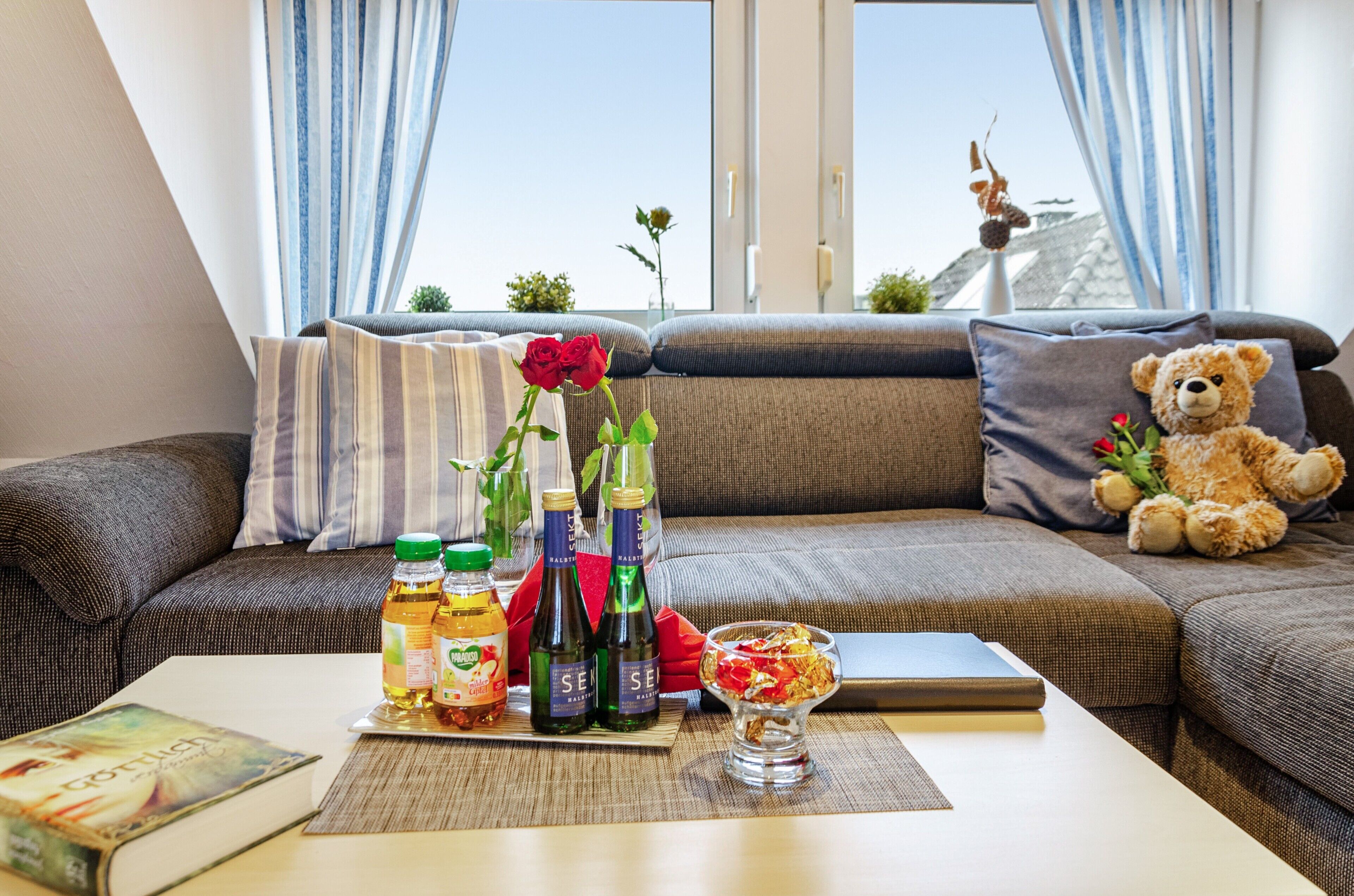En moderne stue med en sofa, en bamse, en rose og flasker på et bord.