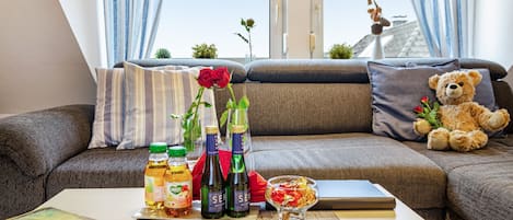 Una sala moderna con un sofá, un osito de peluche, una rosa y botellas sobre una mesa.