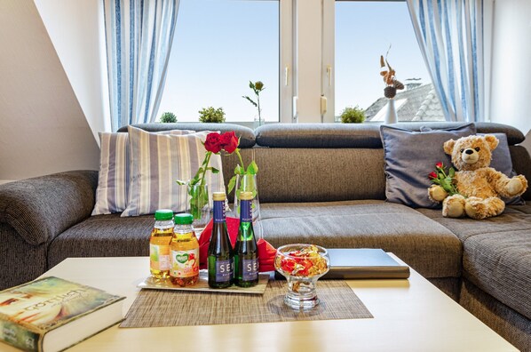 A modern living room with a sofa, a teddy bear, a rose, and bottles on a table.