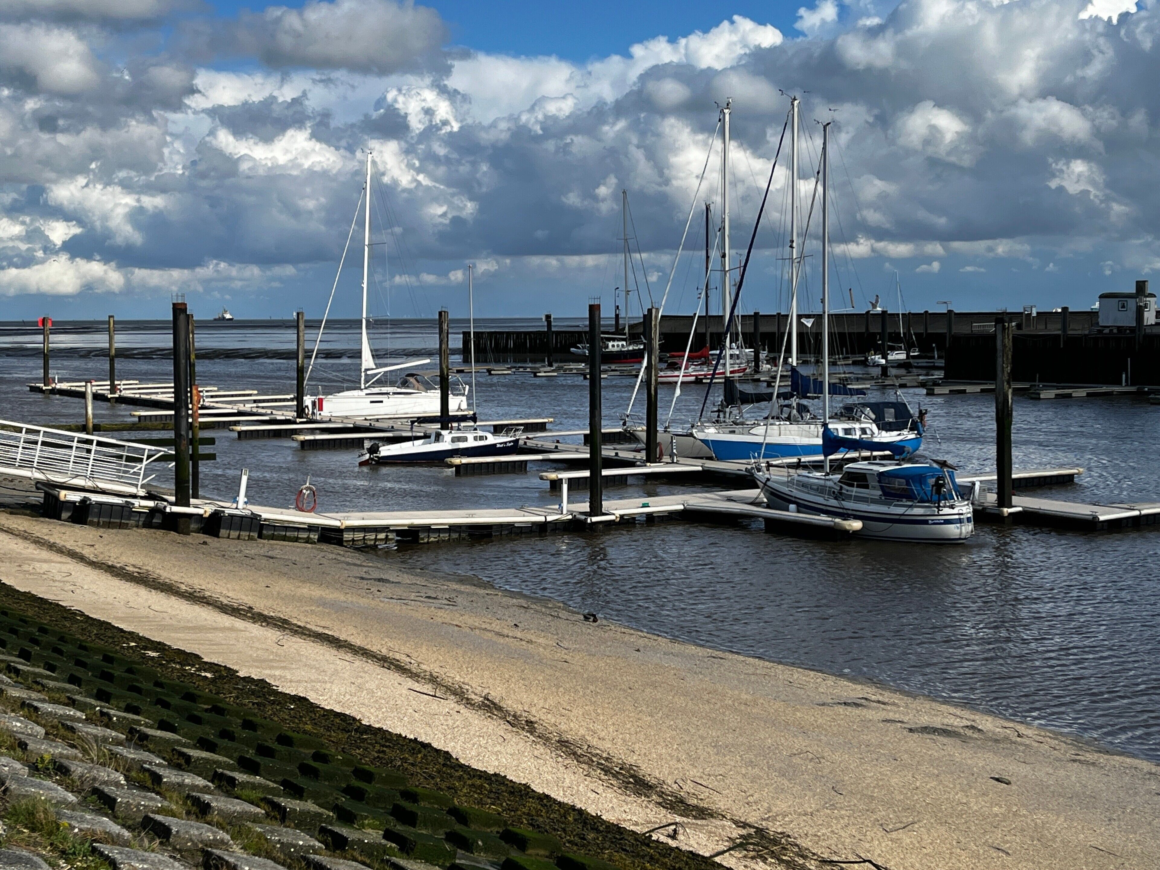 A marina with boats docked at wooden piers, a sandy beach, and a cloudy sky.