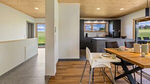 Een moderne keuken met een houten plafond, een eethoek met tafel en stoelen, en uitzicht op een groen veld door een raam.