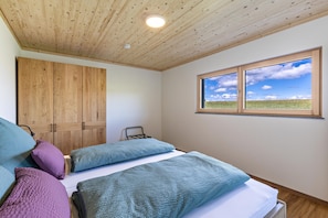 Une chambre avec un plafond en bois, une fenêtre donnant sur un champ et un lit agrémenté de plusieurs oreillers.