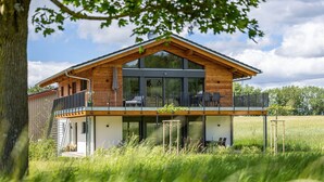 Een modern huis met een groot balkon, ruime ramen en een boom op de voorgrond.