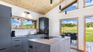 Een moderne keuken met een groot schiereiland, inbouwapparatuur en grote ramen met uitzicht op een groen landschap.