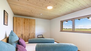 Een slaapkamer met een houten plafond, een groot raam met uitzicht en een bed met kussens.