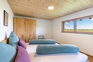 Une chambre avec un plafond en bois, une grande fenêtre donnant sur un beau paysage et un lit avec des oreillers.
