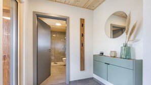 Een moderne badkamer met een glazen douchedeur, een houten accentmuur, een spiegel en een wastafel met een vaas.