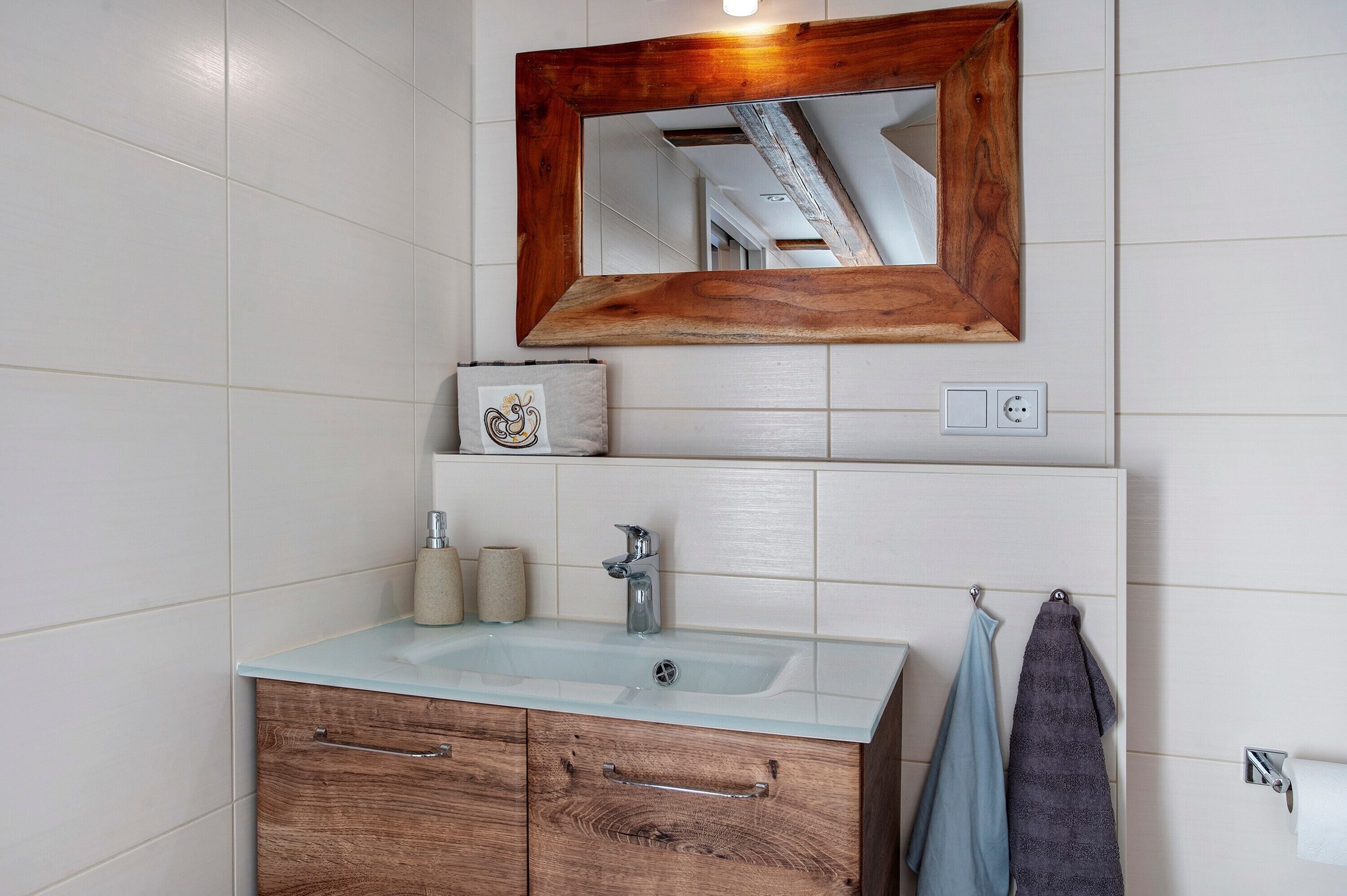 Un baño con tocador de madera, un espejo, un lavamanos y un perchero para toallas.