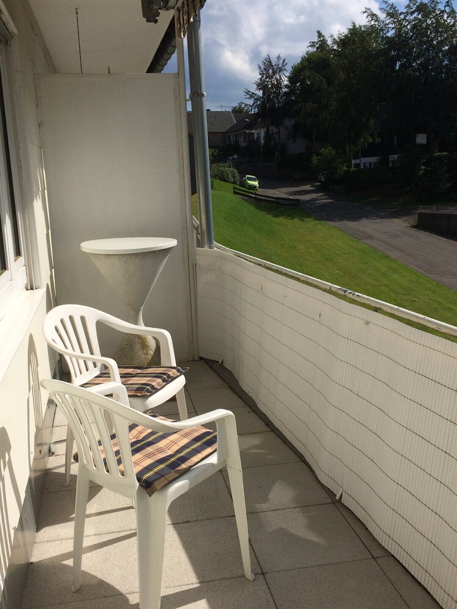 Ein Balkon mit zwei weißen Plastikstühlen und einem kleinen weißen Tisch.