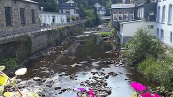 Ein Fluss fließt durch eine Stadt mit Steinhäusern und einem Restaurant namens 'RESTAURANT Alte Herrlichkeit'.