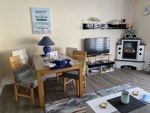 Un salon avec une table en bois, des chaises, un téléviseur, une cheminée et un panneau décoratif au mur.