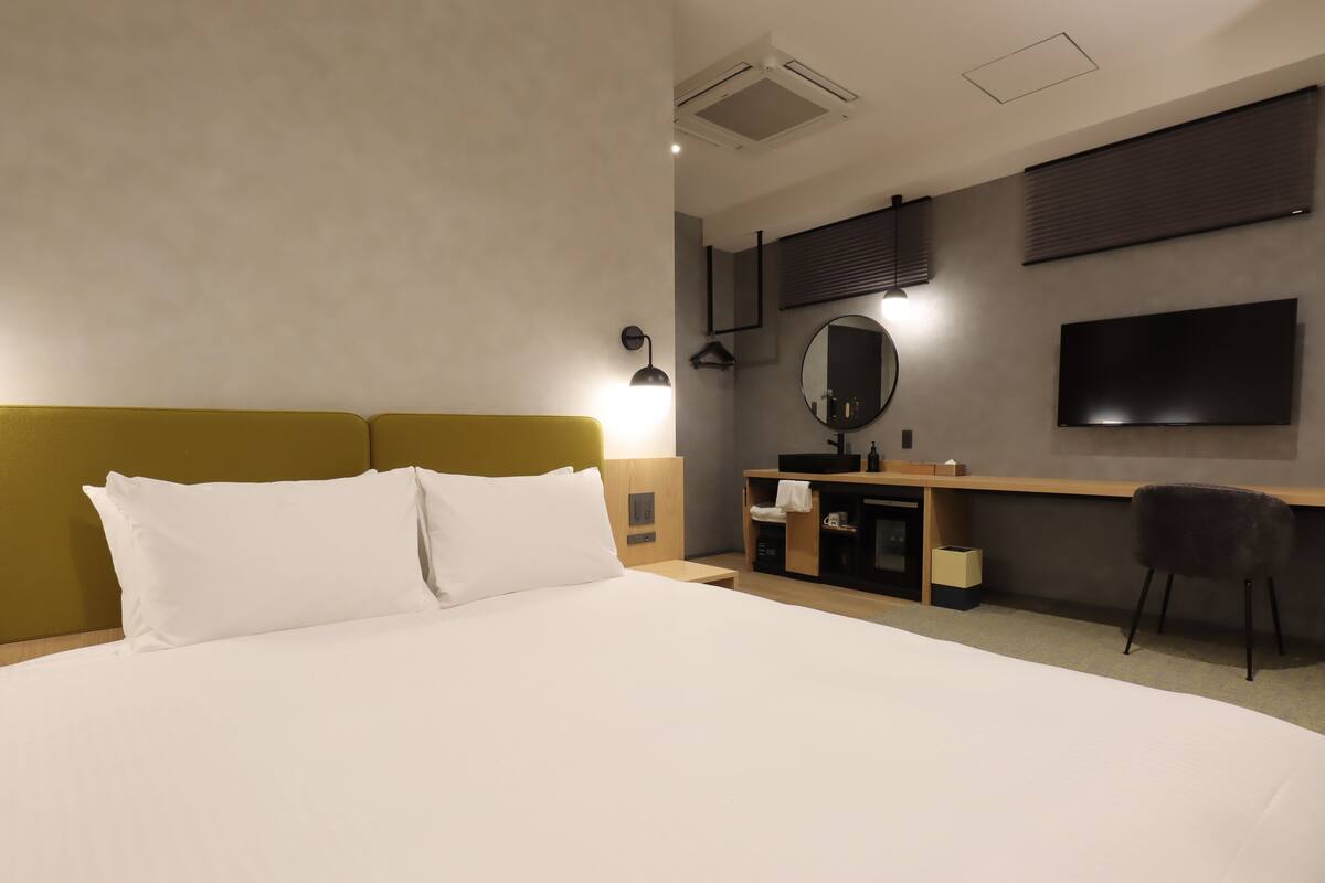 A hotel room with a large bed, a desk with a mirror, a TV, and a chair.