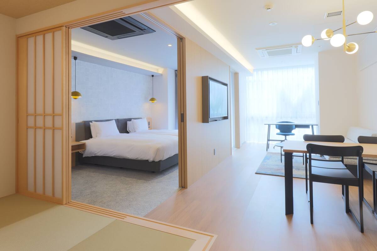 A modern hotel room with a bed, a desk with chairs, and a dining area.
