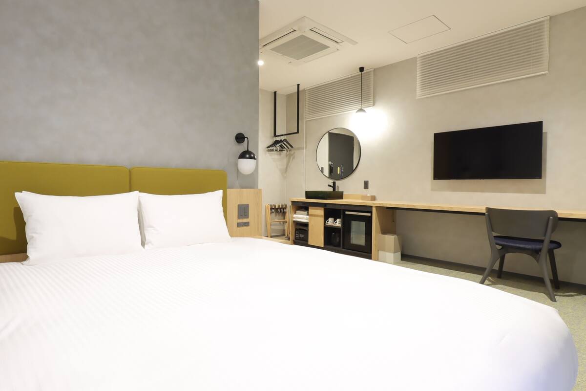 A hotel room with a large bed, a desk with a mirror, a chair, and a television.