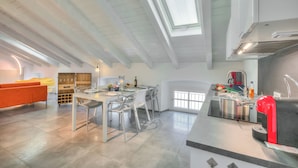A modern kitchen with a skylight, a dining area with a table and chairs, and a bright, airy living space with a sofa and a window. - Loft & Jacuzzi (Riva del Garda)