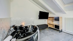 A modern bathroom with a freestanding bathtub, a flat-screen TV mounted on the wall, and a built-in wooden shelf unit. - Loft & Jacuzzi (Riva del Garda)
