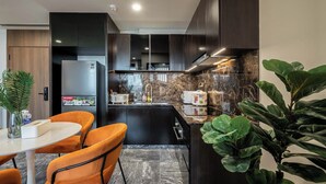 A modern kitchen with dark cabinetry, a built-in refrigerator, and a marble countertop. - The LUMIÈRE Riverside By An Gia Hospitality (Ho Chi Minh City)