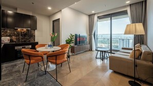A modern living room with a sofa, a dining table with chairs, a TV, and a balcony with a view. - The LUMIÈRE Riverside By An Gia Hospitality (Ho Chi Minh City)