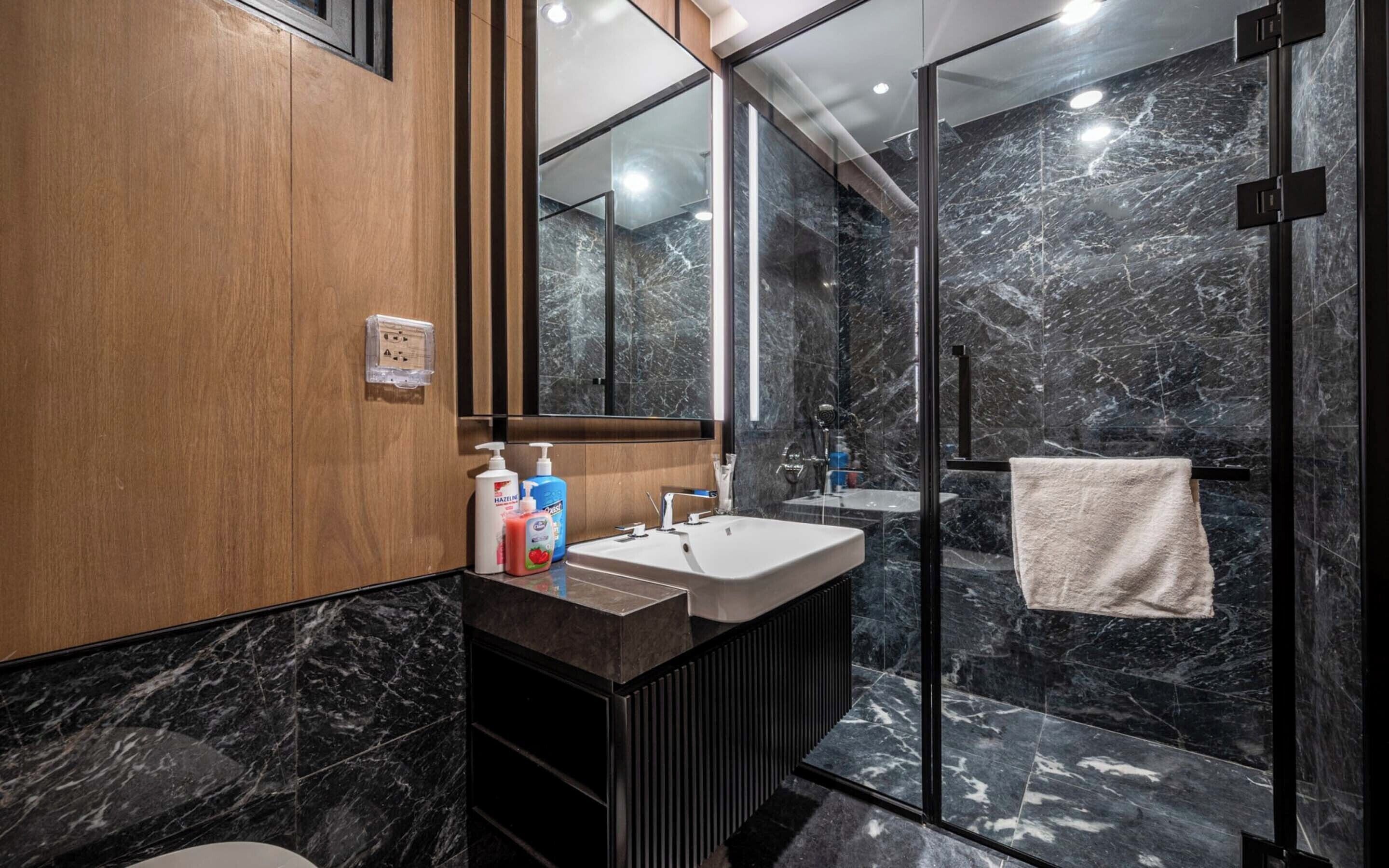 A modern bathroom with a wooden vanity, a glass shower enclosure, and a marble-tiled floor.