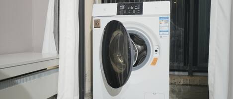 A front-loading washing machine in a room with a tiled floor and a window with curtains.