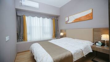 Ein Hotelzimmer mit Bett, Nachttischen, einer Lampe, einer Wand-Klimaanlage und einem Fenster mit Vorhängen.