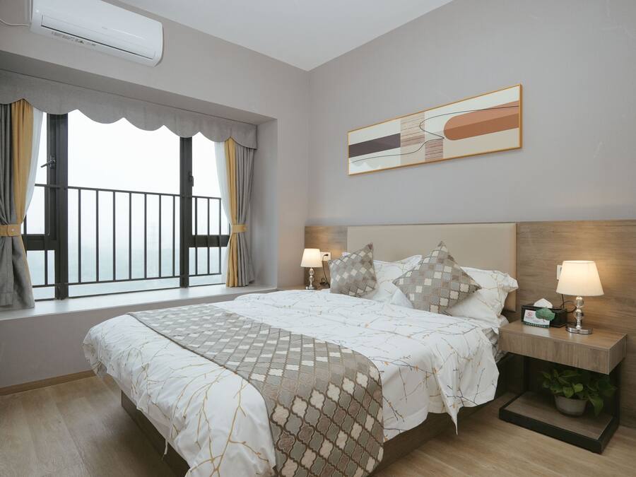 A hotel room with a large bed, two bedside lamps, a nightstand with a plant, and a window with curtains.