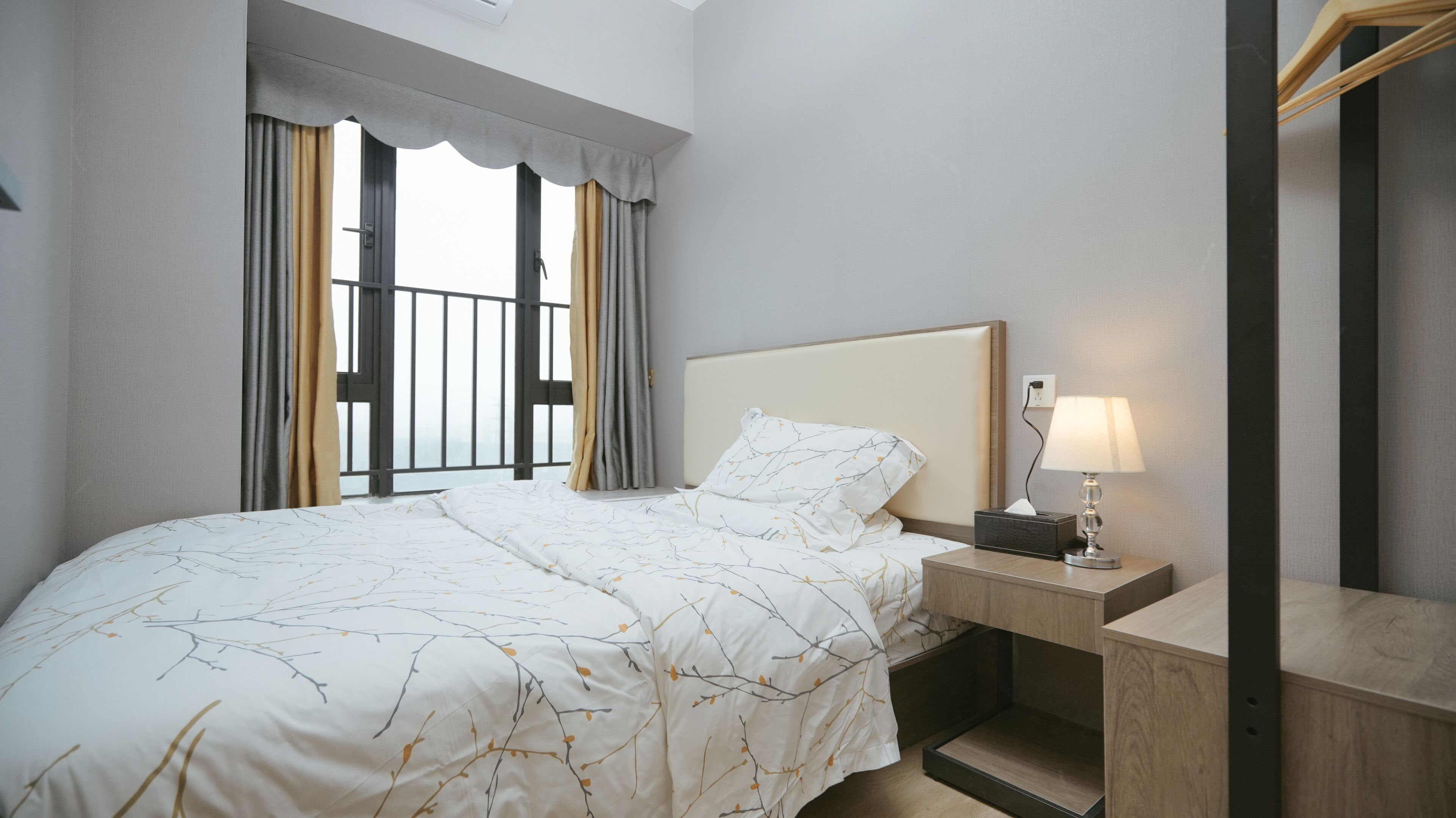 Une chambre d’hôtel avec un lit, une table de chevet avec une lampe, une commode et une fenêtre avec des rideaux.